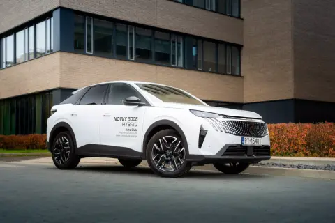 Biały Peugeot 3008 hybryda plug-in zaparkowany przed nowoczesnym budynkiem.