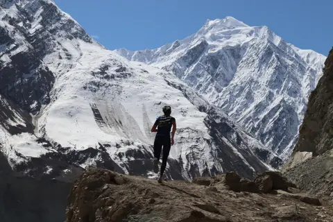 Perrine Fages court sur un sentier rocailleux face à des montagnes enneigées majestueuses sous un ciel bleu éclatant.