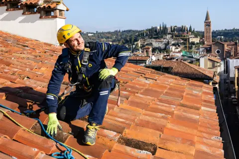 Operaio in corda per la riparazione tetto casa, con vista panoramica sulla città.