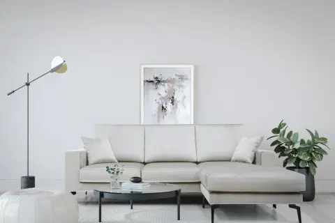 Divano angolare color crema, con tavolino rotondo in vetro, pouf bianco e quadro astratto. Le misure divano angolare sono perfette per questo spazio.