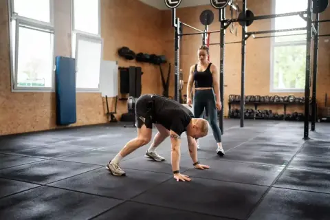 Mężczyzna wykonuje burpee pod okiem trenerki w siłowni.