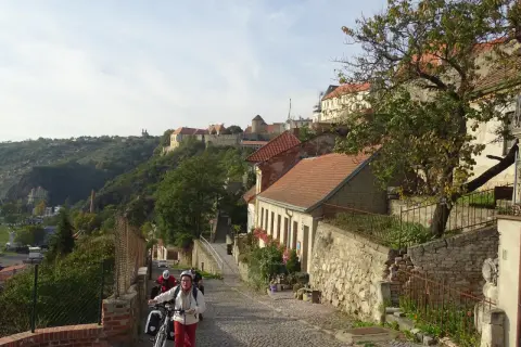 Radfahrer erkunden eine Kopfsteinpflasterstraße in Znaim, Tschechien, mit historischen Gebäuden und einer Burgruine im Hintergrund.