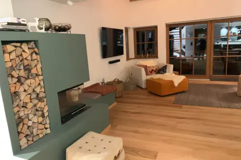 Gemütliches Wohnzimmer im modernen Landhausstil mit Kamin, Holzfußboden und großen Glasfronten.