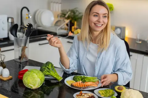 Femme souriante dégustant un menu équilibré pour perdre du poids : saumon, brocolis, avocat, noix et légumes frais.