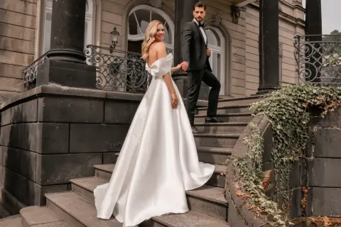 Brautpaar auf Treppe, sie trägt ein elegantes weißes schleppe brautkleid, er im schwarzen Anzug.