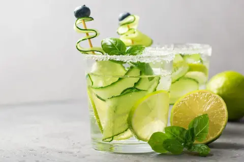 Zwei erfrischende Aperitifs mit Gurke, Limette und Minze, garniert mit Blaubeeren.