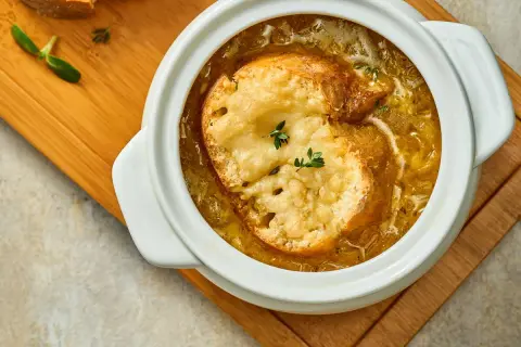 Soupe à l'oignon grand mère réconfortante, gratinée avec du pain et du fromage fondant, servie dans un bol blanc sur une planche en bois.