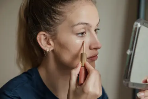Ragazza applica correttore sotto l'occhio, un passo per capire il colore del correttore online.