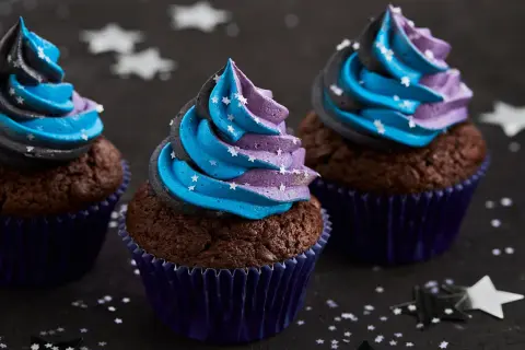 Drei Schoko-Cupcakes mit blau-lila Sternen-Frosting, inspiriert von einem Galaxie-Cupcake-Rezept.