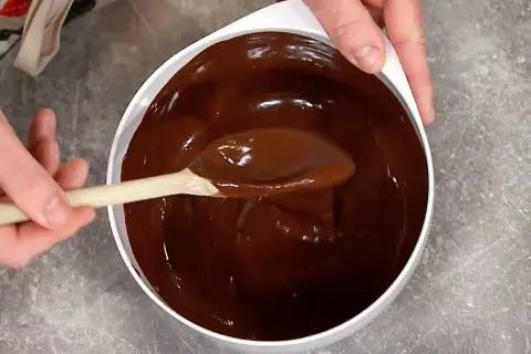 En sked rör i en skål med glansig choklad. Perfekt för ett enkelt ganache recept.