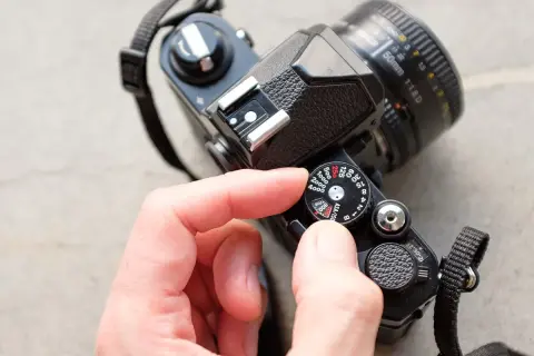 A hand adjusts the ISO dial on a vintage film camera, showing its mechanical controls.