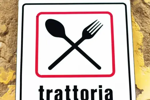 Segnale con forchetta e cucchiaio incrociati, che indica una trattoria. Un invito a gustare sapori autentici, diverso dall'osteria.
