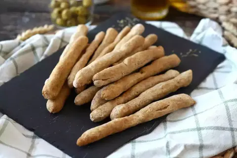 Une pile de gressins dorés, parfaits pour une recette gressin maison. Des olives et une boisson en arrière-plan.