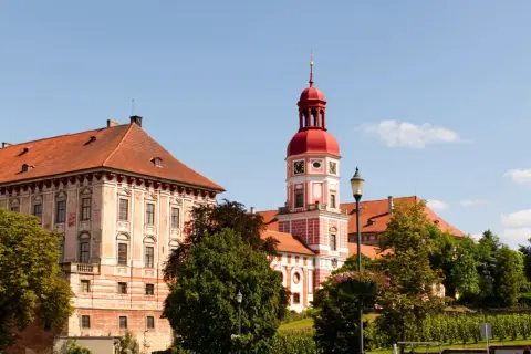 Schloss Roudnice nad Labem mit seinem roten Turm und den Ziegeldächern, umgeben von grünen Bäumen.