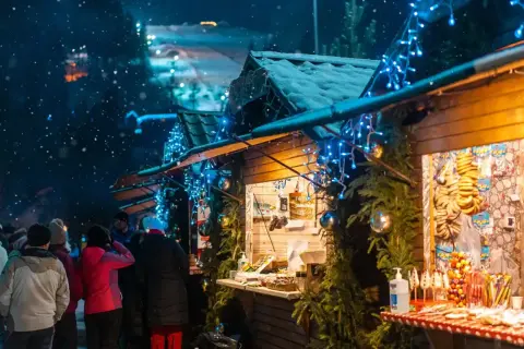 Mercatini di Natale nelle Marche: bancarelle illuminate da lucine blu, neve che cade e gente che passeggia tra gli stand.