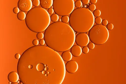 Orangefarbene Bläschen, wie von Butylmethoxydibenzoylmethan, schweben auf einem warmen, orangen Hintergrund.