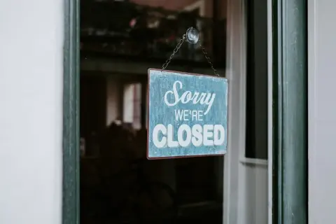 En blå skylt med texten "Sorry WE'RE CLOSED" hänger i ett fönster. Enskild firma i vilande.