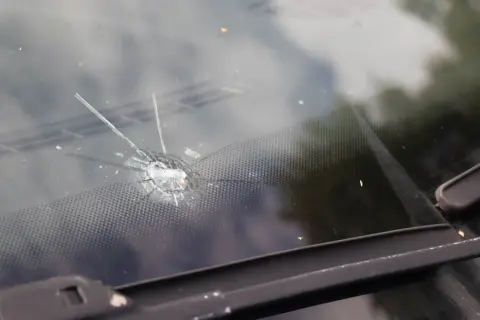 Odprysk na przedniej szybie samochodu, przypominający gwiazdę, z widocznymi pęknięciami i drobnymi odłamkami szkła.