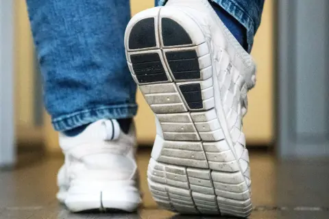 Nahaufnahme von weißen Turnschuhen mit Jeans. Die Sohle eines Schuhs ist deutlich zu sehen, bereit für den nächsten Schritt, der vielleicht quietschende Schuhe hinterlässt.