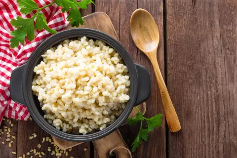 Kasza bulgur w czarnej misce, obok drewniana łyżka i natka pietruszki. Niska kasza bulgur indeks glikemiczny.
