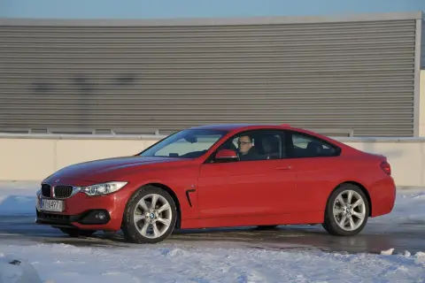 Czerwone BMW F32 435i z kierowcą za kierownicą, zaparkowane na śniegu przed budynkiem.
