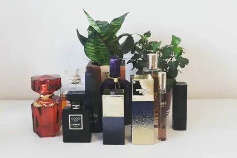 Kolekcja perfum: czerwony Chopard, czarny Coco Noir Chanel 100ml, fioletowy i złoty Michael Kors, oraz inne, otoczone zielenią.