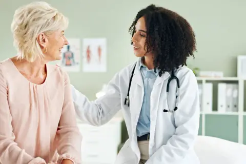 Ärztin mit Stethoskop legt Hand tröstend auf Schulter einer Patientin. Ein Gespräch über gynäkoonkologische Themen findet in einer freundlichen Atmosphäre statt.