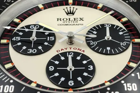 En närbild av en Rolex Daytona, en ikonisk klocka som Paul Newman själv bar. Den har tre svarta urtavlor på en krämfärgad bakgrund.