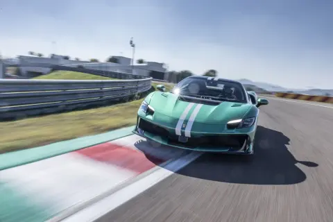 Zielony Ferrari 296 GTB z białymi pasami pędzi po torze wyścigowym, zostawiając za sobą rozmyte tło.