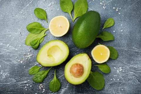 Awokado, cytryna i szpinak na ciemnym tle. Niska wartość indeksu glikemicznego awokado czyni je idealnym składnikiem zdrowej diety.