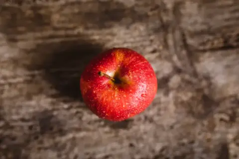 Czerwone, lśniące jabłko z kroplami wody na drewnianym tle. Niskie jabłko indeks glikemiczny to zdrowa przekąska.