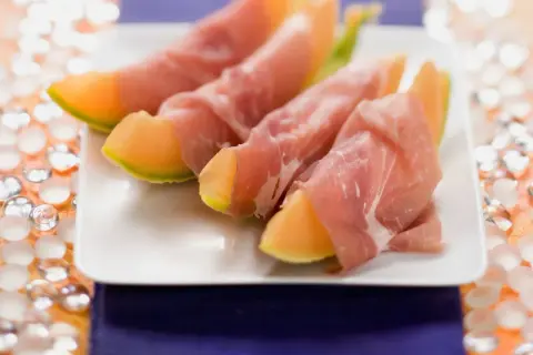 Saftige Honigmelone mit zartem Schinken umwickelt, serviert auf einem weißen Teller. Ein süß-salziger Genuss!