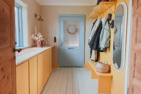 Warme Farben und natürliche Materialien prägen diesen Flur. Farbgestaltung Flur Tapeten Beispiele: Gelbe Schränke, Holzboden, Garderobe mit Jacken.