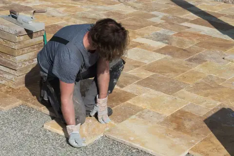 Un ouvrier pose des dalles de travertin pour créer une terrasse.