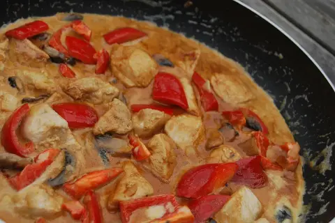 En smakrik chicken karahi i en panna med möra kycklingbitar, röd paprika och champinjoner i en krämig sås.