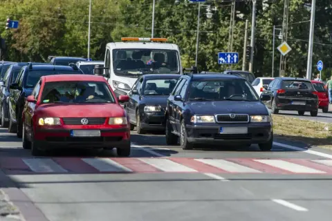 Korki na drodze, kierowcy próbują omijanie stojących aut. Czerwony Volkswagen i granatowa Skoda czekają na zielone światło.
