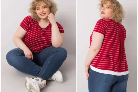 Kobieta plus size w czerwonej bluzce w paski i jeansach siedzi na podłodze.