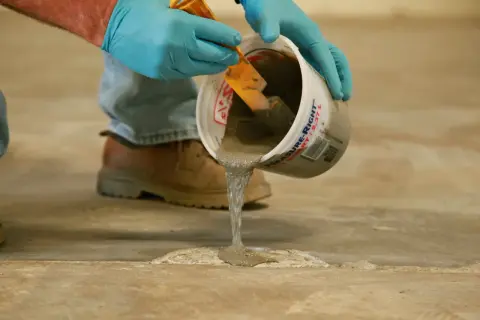Man con guantes azules vierte mortero para reparación de fisuras en soleras de hormigón.