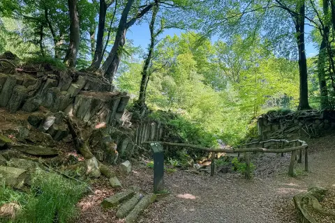 Ein Pfad führt durch einen Wald mit steilen Felsformationen. Ein blauer Stein liegt am Wegesrand.