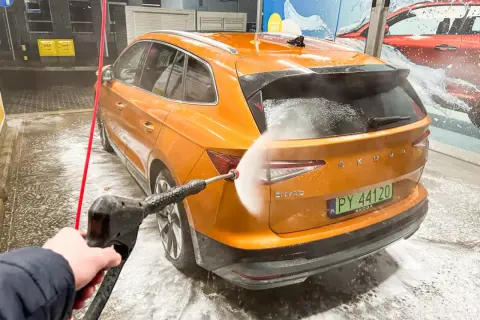 Pomarańczowy Skoda Enyaq jest myty na myjni bezdotykowej. Woda pod ciśnieniem spływa po karoserii, tworząc pianę.