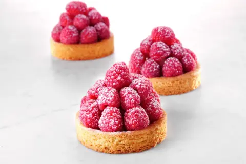 Trois tartelettes sablé breton garnies de framboises fraîches saupoudrées de sucre glace. Une invitation à la gourmandise.