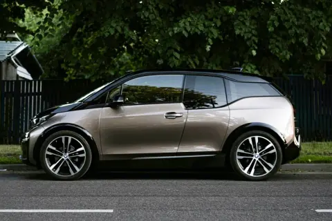 En BMW i3 står parkerad vid en grönskande trädgård. Kanske ett problem med laddningen?