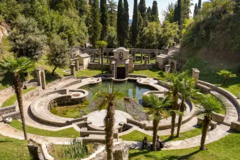Un incantevole giardino botanico sul Lago di Garda, con un laghetto circondato da architetture in pietra e palme.