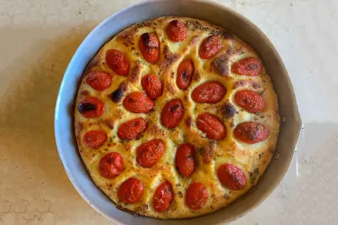 Focaccia foggiana dorata e fragrante, con pomodorini succosi e erbe aromatiche, pronta per essere gustata.