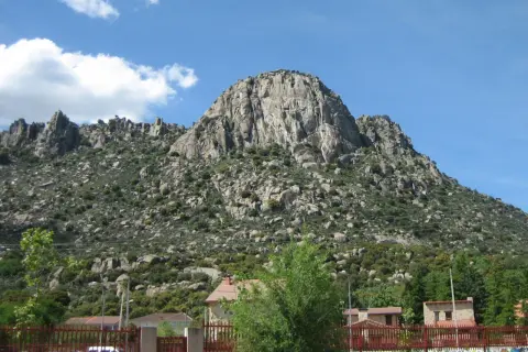 Majestuosa sierra de la Cabrera, con sus rocas imponentes y vegetación verde, bajo un cielo azul con nubes blancas.