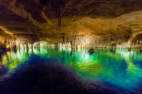 Magiska grottor på Mallorca med turkost vatten som reflekterar stalaktiter och stalagmiter. En båt anas i bakgrunden.