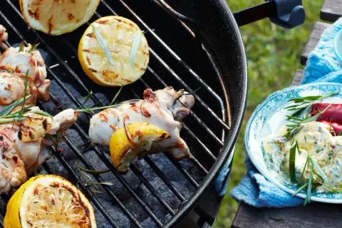 Grillad kyckling med citron och rosmarin på grillen. En tallrik med kycklingröra, chili och örter står bredvid.