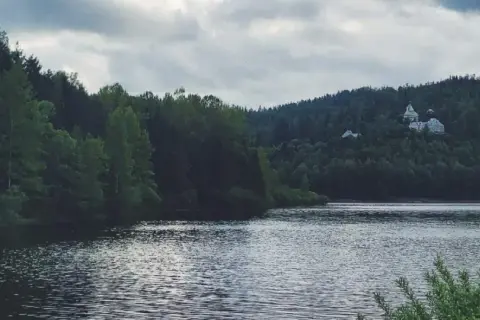 Spokojne jezioro Czerniańskie otoczone gęstym lasem, z widocznym na wzgórzu pałacem.