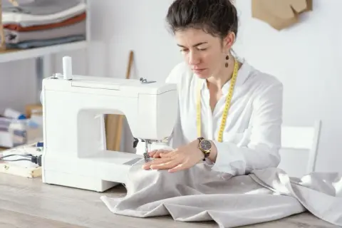 Krawcowa pracuje przy maszynie, dobierając odpowiednie rozmiary igieł do tkaniny.