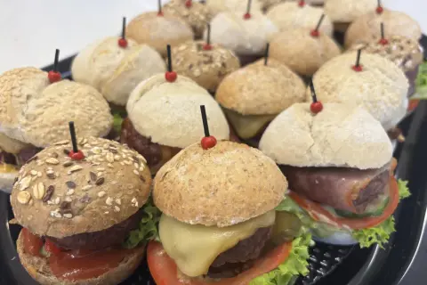 Mini hamburgery gdzie kupić? Taca pełna pysznych, małych burgerów z serem, warzywami i różnymi bułkami. Idealne na imprezę!